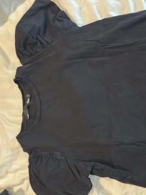 Svart topp med puffärmar från lager 157 - En svart topp från lager 157 med puffiga korta ärmar och rund halsringning. Tillverkad i mjuk bomull som känns skön mot huden. Enkel och stilren design som passar till många olika looks.