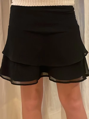 Svart volangkjol från Gina Tricot - Säljer en svart kortkjol från Gina Tricot med dubbla volanglager. Kjolen har en mjuk resår i midjan.🩷 