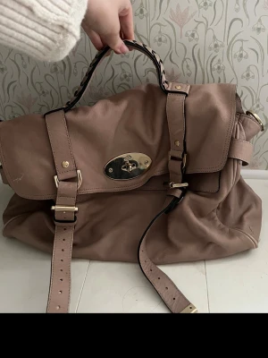 Beige Mulberry axelväska i skinn - Säljer en beige axelväska från Mulberry i mjukt skinn. Väskan har flätat handtag, guldiga metalldetaljer och klassiskt vridlås framtill. Invändigt finns mönstrat foder med Mulberry-loggor och flera fack med dragkedja. Perfekt för dig som vill ha både stil och funktion. pris kan diskuteras. 