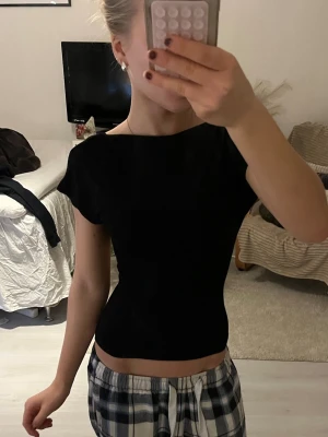 Svart topp med öppen rygg - Säljer en svart, tight topp med korta ärmar och öppen rygg. Toppen har en enkel och stilren design som sitter figurnära och är perfekt för dig som gillar minimalistiska plagg med en twist. Materialet känns mjukt och stretchigt. 