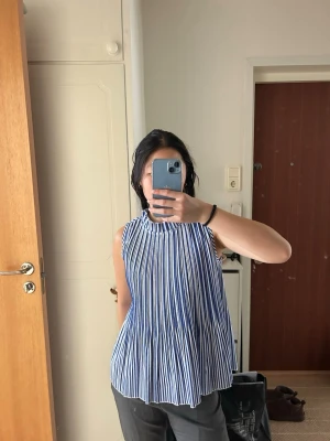 Randig blåvit ärmlös blus från Estampa - Säljer en luftig och plisserad ärmlös blus från Estampa i storlek S. Toppen har blå och vita vertikala ränder, hög krage och ett flowy fall. Har aldrig kommit till användning tyvärr
