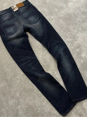 Mörkblåa Nudie jeans - Sällsynta mörkblå Nudie jeans med gråaktig wash. Topp skick, knappt använda. Slim/straight passform, slitstarkt och bekvämt material. Perfekta för vardag eller fest.