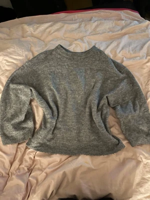 Grå stickad tröja från 157 - Mysig grå stickad tröja från 157 i storlek M. Tröjan har en klassisk rund halsringning och långa ärmar med ribbade muddar. Perfekt för lager-på-lager och chill dagar. Enkel att matcha med jeans eller kjol.