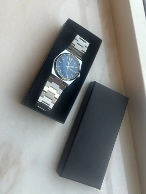 Klocka  - Bilderna visar en klocka i metall med blå urtavla och länkarmband, klockverktyg finns med 