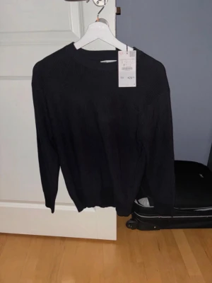Svart stickad tröja från Zara - Säljer en svart stickad tröja från Zara i storlek S. Tröjan har rund halsringning, ribbade muddar och är långärmad. Perfekt för lager-på-lager och enkel att matcha med jeans eller kjol. Den är helt ny då den aldrig är använd.