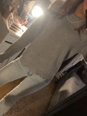 Grå stickad tröja med rund hals - En enkel och stilren grå stickad tröja med rund halsringning. Tröjan har långa ärmar och ribbade muddar vid ärmslut och nederkant. Perfekt att matcha med jeans för en chill look.