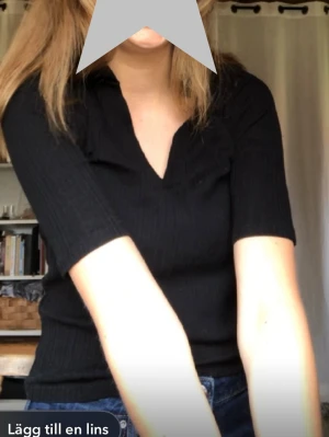 Svart ribbad topp från Lindex - Säljer en svart ribbad topp från Lindex med krage och v-ringning. Toppen har trekvartsärm och är i ett stretchigt material.