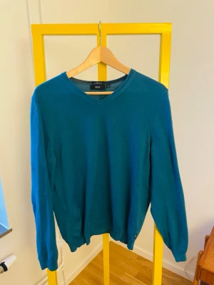 Blå merinoullströja från Hugo Boss - Snygg blå tröja från Hugo Boss i extrafin merinoull. Slim fit-modell med v-ringning och långa ärmar. 