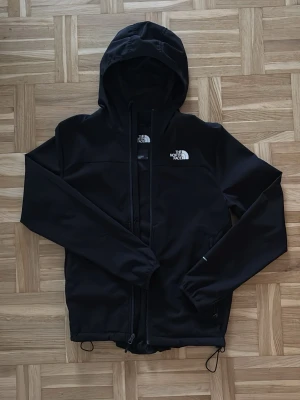 The North Face tunn jacka – svart - Svart tunn jacka från The North Face. Perfekt som vår/höstjacka eller som lager-på-lager. Jackan är i fint skick, sparsamt använd och utan hål eller fläckar. Dragkedja framtill och huva. Stilren och lätt modell.
