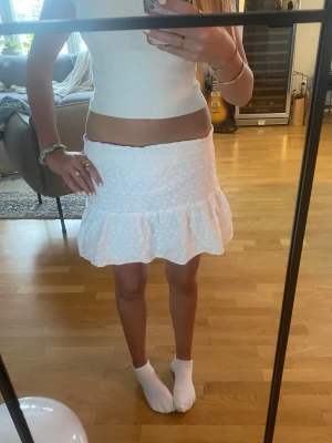 Vit kortkjol med volang - Supersöt vit kortkjol från New Yorker med broderade små blommor och bred resår i midjan. Kjolen har en volangkant nedtill som ger en luftig och somrig känsla. Perfekt att matcha med en crop top eller linne för en fräsch look.