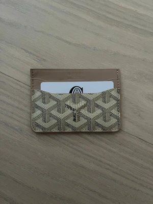 Beige plånbok med mönster - Säljer en beige och brun kortplånbok  med deras ikoniska grafiska mönster. Plånboken har flera kortfack och är tillverkad i skinn med snyggt tryckt logga och detaljer. Perfekt för dig som vill ha något stilrent och lyxigt i fickan.