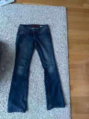 Mörkblå bootcut jeans  - Säljer ett par mörkblå bootcut jeans  med snygga slitningar och klassiska fem fickor. Jeansen har låg midja och är tillverkade i mjukt denimtyg. Perfekta för dig som gillar en avslappnad men ändå trendig look. De är ganska små midjan, skriv för mått