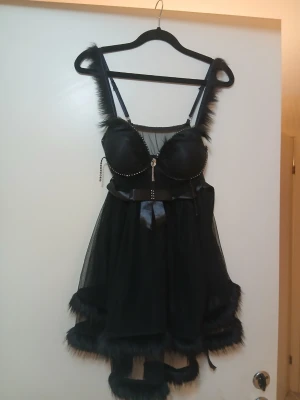 Svart och leopardmönstrad pälsväst - Två unika västar med fluffiga pälsdetaljer på axelband och nederkant. Ena västen är helsvart med mesh och satinrosett, den andra har leopardmönster upptill och transparent tyg nedtill. Båda har dekorativa stenar och band framtill för extra bling.