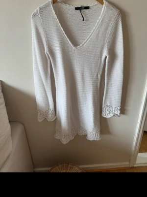 Vit stickad kortklänning med spets - Supersöt vit stickad kortklänning från Bik bok med v-ringning och långa ärmar. Klänningen har fina spetsdetaljer vid ärmslut och nederkant som ger en romantisk vibe. Perfekt till sommaren eller våren!