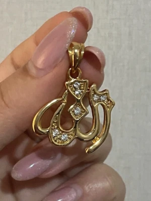 Guldfärgat hänge med stenar ”Gud” på arabiska ✨ - Säljer ett guldfärgat hänge där det står gud på arabiska, dekorerat med gnistrande stenar. Hänget har en snygg, rundad form och blanka ytor som ger en lyxig känsla. Perfekt att bära i en kedja för en personlig touch. 