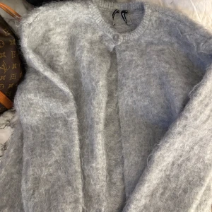 Grå mohair kofta från BikBok - Supermjuk och fluffig grå kofta från BikBok i mohair- och ullblandning. Koftan har rund halsringning, knapp framtill och lång ärm. Perfekt för lager-på-lager och ger en mysig vibe till din outfit. Oanvänd utan prislapp!!🤍pris kan diskuteras!