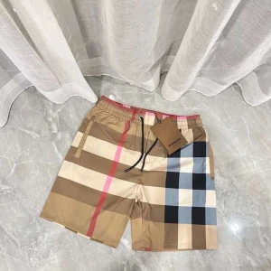 Burberry shorts med snörning - Snygga shorts från Burberry med klassiskt rutigt mönster i beige, svart, vit, blå och röd. De har elastisk midja med snörning och fickor på sidorna samt en bakficka. Perfekta för sommaren och ger en lyxig vibe till din outfit.