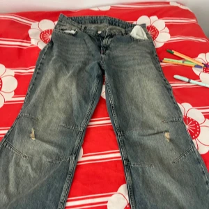 Blå bootcut jeans med slitningar - Säljer ett par blå jeans med bootcut-modell och coola slitningar på knäna. Jeansen har klassisk femficksdesign och är tillverkade i jeansmaterial. Perfekt för dig som gillar en avslappnad och trendig stil.