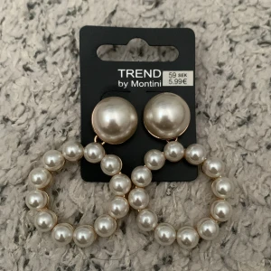 Pärlörhängen från Montini - Stora statement-örhängen från Montini med rund form och glansiga vita pärlor. Örhängena har en klassisk look med pärlor både på knoppen och i en cirkel nedanför. Perfekta för att lyfta vilken outfit som helst. Helt nya!