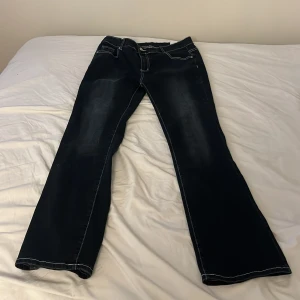 Mörkblå bootcut jeans med broderi - Snygga mörkblå jeans med bootcut passform och vita kontrastsömmar. Bakfickorna har detaljerade broderier i vitt och grått som ger en unik look. Jeansen har klassisk femficksdesign och är tillverkade i jeansmaterial.