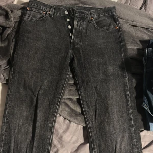 Levi's 501 svarta jeans straight fit - Svarta Levi's 501 Premium jeans med klassisk knappgylf och raka ben. Jeansen har fem fickor, silverfärgade knappar och en snygg tvättad finish. Är i storlek W 29 och L 32 och är regular fit.