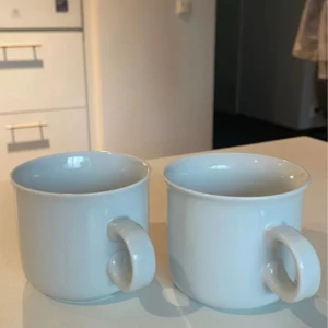 Vit mugg - Två vita porslinsmuggar i klassisk design. Muggarna är i fint skick utan synliga sprickor eller nagg. Perfekta för kaffe eller te och passar i de flesta kök. Säljs som ett set om två stycken.
