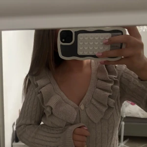 Beige kofta med volang och kabelstickning - Superfin beige kofta med kabelstickat mönster och stora volanger längs v-ringningen. Koftan har långa ärmar och knäpps framtill med dekorativa knappar. Perfekt för dig som vill ha en söt och trendig look💞skickar gärna lite fler bilder till den som är intresserad! 