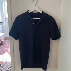 Mörkblå pikétröja från Bondelid - Snygg mörkblå pikétröja från Bondelid i klassisk modell med krage och knappar framtill. Tröjan är i bomull och har diskret broderad logga på bröstet. Perfekt för en clean och stilren look.