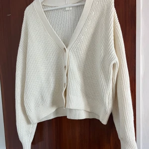 Beige stickad kofta från H&M - Mysig beige stickad kofta från H&M med v-ringning och knappar framtill. Koftan har en loose passform, ribbade muddar och långa ärmar. Perfekt att slänga över en t-shirt eller linne när det är kyligt ute. En fläck på tröjan (se bild)