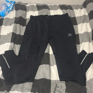 Svarta täckbyxor X-Trail XL med dragkedja - Svarta täckbyxor från X-Trail i storlek XL. Byxorna har elastisk midja och dragkedjor vid bensluten för enkel av- och påtagning. Perfekta för kalla dagar och utomhusaktiviteter. Snygg och sportig design med diskret logga på benet. (Ignorera städservetterna i bilden) :)