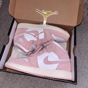 Nike Air Jordan 1 Mid rosa/vit - Säljer ett par Nike Air Jordan 1 Mid i en snygg kombination av ljusrosa mocka och vitt skinn. Skorna har klassisk snörning, perforerad tå och ikoniska Jordan-detaljer. Perfekta för dig som vill sticka ut med stilrena sneakers i pastelltoner. Använd en gågn men kommer inte mer till anständig. 