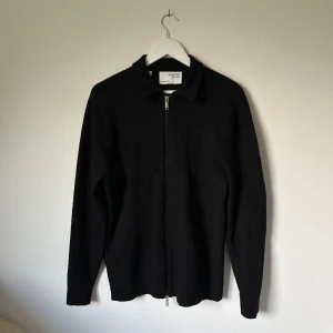 Svart merinoullskofta från Selected Homme - Svart kofta i 100% merinoull från Selected Homme. Klassisk rak modell med krage och hel dragkedja framtill. Långärmad och enkel design som funkar till många olika stilar. Perfekt för lager-på-lager under kyliga dagar. 3X2