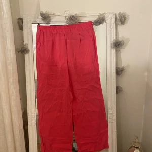 Rosa vida byxor från ONLY - Säljer ett par rosa byxor från ONLY med resår i midjan och avslappnad, vid passform. Byxorna är tillverkade i ett lätt material som känns luftigt och skönt. Perfekta för dig som gillar en chill och trendig look.