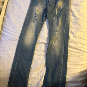 Dsquared2 ljusblå slitna jeans slim fit - Säljer ett par ljusblå jeans från Dsquared2 i modellen K-110 Slim Fit. Jeansen har slitna detaljer och snyggt tvättad look, klassisk femficksdesign och normal midja. Materialet är jeans i bomull och passformen är slim. Perfekta för dig som gillar en trendig och avslappnad stil.