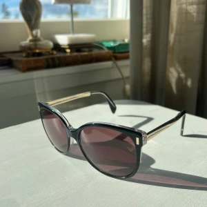 Solglasögon Marc by Marc Jacobs - Snygga solglasögon från Marc by Marc Jacobs med svarta bågar och guldiga skalmar. Modellen är MMJ 464/S A52HD storlek 56 17 135 V. Smärre tecken på användning. Fraktas i fodral.