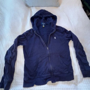 Marinblå hoodie från Polo Ralph Lauren - Säljer en marinblå hoodie från Polo Ralph Lauren med dragkedja och huva. Passar dig som är runt 150-160, passar perfekt för hösten/våren. Hör gärna av dig vid intresse för fler bilder eller info😊
