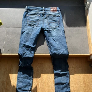 Blå jeans från Hollister - Säljer ett par blå jeans från Hollister med klassisk femficksdesign och snygga kontrastsömmar. Jeansen har normal midja och är tillverkade i stretchig denim för en tight passform. Perfekta för dig som gillar en smal siluett och stilren look.