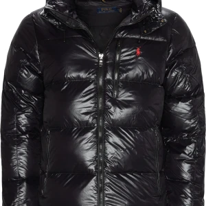 Svart pufferjacka från Polo Ralph Lauren - Snygg svart pufferjacka från Polo Ralph Lauren med glansig finish och röd logga på bröstet. Jackan har huva, flera dragkedjefickor och quiltad design som håller värmen. Perfekt för kalla dagar och riktigt stilren look. PRISET KAN DISKUTERAS!!❣️