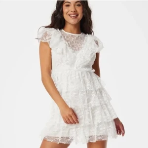 Vit spetsklänning från Bubbleroom - Supersöt vit kortklänning från Bubbleroom med flera lager volanger och spetsdetaljer. Klänningen har v-ringad front, transparent spets upptill och korta ärmar. Perfekt som studentklänning. Storlek M. Endast använd en gång.