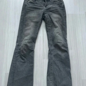 Grå bootcut jeans från Gina Tricot - Snygga grå jeans från Gina Tricot i bootcut-modell. Jeansen har klassiska fem fickor, dragkedja och knapp framtill samt coola detaljer på bakfickorna. Perfekt för dig som gillar en avslappnad men trendig look.