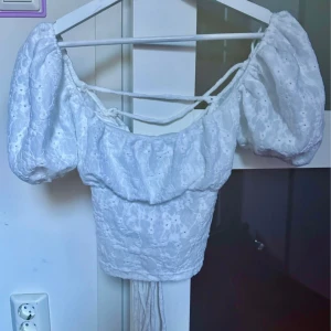 Vit spetsblus med puffärm från Zara - Superfin vit blus från Zara med puffiga korta ärmar och snörning i ryggen. Blusen har broderade spetsdetaljer och är croppad, perfekt till höga jeans eller kjol. Söt och romantisk vibe med offshoulder-modell och fina detaljer.