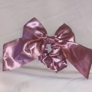 Rosa satin diadem med stor rosett - Superfint diadem i glansig rosa satin med en stor, iögonfallande rosett. Perfekt accessoar för att lyfta din look med en söt och trendig touch. Sitter bekvämt och ger en extra pop till håret.