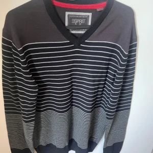 Randig svart tröja från Esprit - Snygg100% bomull svart tröja från Esprit med vita horisontella ränder och v-ringad hals. Tröjan har långa ärmar och ribbade muddar. Perfekt för dig som gillar en stilren och klassisk look.