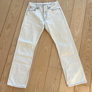 Vita Levi's 501 jeans W32 L - Säljer ett par klassiska vita Levi's 501 jeans med raka ben och femficksmodell. Jeansen har tydliga kontrastsömmar och den ikoniska läderpatchen bak i midjan. Perfekta för dig som vill ha en clean och tidlös look.