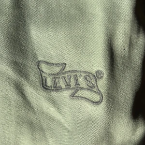 Grå Levi's Red Tab jeansjacka S - Snygg grå jeansjacka från Levi's Red Tab i storlek S. Jackan har coola detaljer som broderad logga på ärmen, stora fickor med knappar och ribbad mudd nedtill. Klassisk krage och markerade sömmar ger en streetig vibe. Perfekt för dig som gillar en avslappnad men stilren look.