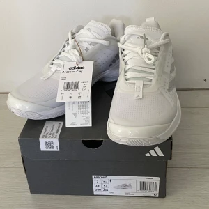 Adidas Avacourt vita tennisskor - Adidas Avacourt vita tennisskor med snygg, sportig design. Skorna har snörning, ventilerande mesh och detaljer i syntet. Lätta och flexibla med Torsion System-sula för extra stabilitet. Perfekta för tennisbanan och tillverkade med fokus på hållbarhet.