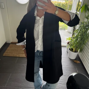 Svart rock i klassisk modell - Stilren svart rock med rak passform och stora fickor framtill. Jackan har enkel knäppning och är perfekt för dig som gillar en clean och tidlös look. Passar snyggt över skjorta eller hoodie och funkar året runt.