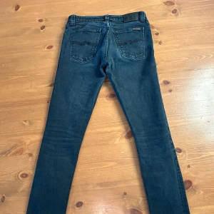 Mörkblå jeans från Nudie - Snygga mörkblå jeans från Nudie Jeans med klassisk femficksdesign och svarta broderade detaljer på bakfickorna. Jeansen har normal midja och är tillverkade i bomullsdenim för en bra passform.