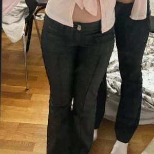 Svarta bootcut byxor med fickdetaljer - Snygga svarta bootcut byxor med markerad söm framtill och dubbla knappar i midjan. Byxorna har fickor med lock framtill och klassiska bakfickor. Materialet är stretchigt och ger en tight passform upptill med utsvängda ben nertill🩷🩷 