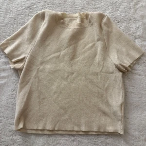 Beige stickad kortärmad tröja - En stilren beige stickad tröja med korta ärmar och rund halsringning. Perfekt för lager-på-lager eller som den är under varmare dagar. Enkel och clean design som passar till det mesta.